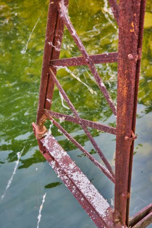 Photo for Image of Textured and rusty bridge part with crisscrossing thin metal beams over river water with cobwebs - Royalty Free Image