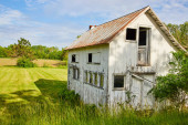 Image of Abandoned farm house in grassy field near farmland with busted windows and door puzzle #667387434