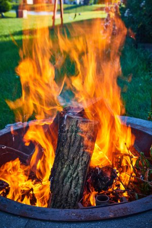 Image of Backyard fire pit with green lawn in round pit with tall orange and yellow flames
