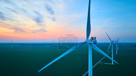 Photo for Image of Green farmland with rows of wind turbines on wind farm aerial at gorgeous pink and orange sunset - Royalty Free Image