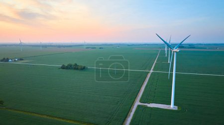 Photo for Image of Aerial row of wind turbines in green farmland fields at sunrise or sunset with orange and pink sky - Royalty Free Image