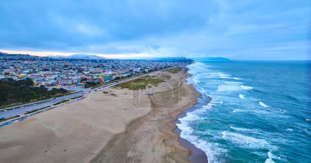 Téléchargez les photos : Image de Large antenne de rivage de plage de sable avec des vagues océaniques à droite et une ville à gauche - en image libre de droit