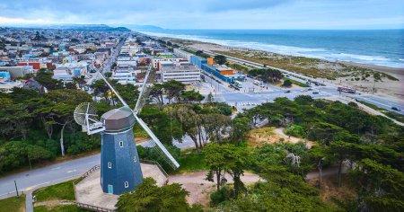 Téléchargez les photos : Image du moulin à vent murphy bleu aérien avec pales blanches surplombant la ville de tuyaux et l'océan avec plage - en image libre de droit