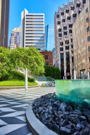 Photo for Image of Park with unique glass wall with water running down sides toward rocks and checkered sidewalk - Royalty Free Image
