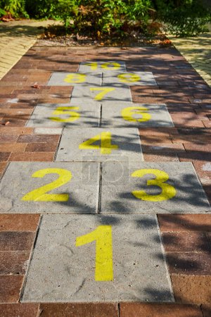 Photo for Image of Hopscotch kids game on brick path with yellow numbers and shadow of leaves on sidewalk - Royalty Free Image