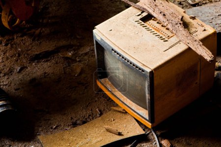 Téléchargez les photos : Un téléviseur abandonné CRT, recouvert de rouille et de débris, se trouve sur un sol sale dans la délabrée usine Pierceton, Indiana. L'éclairage sombre met en évidence son obsolescence et le passage de - en image libre de droit