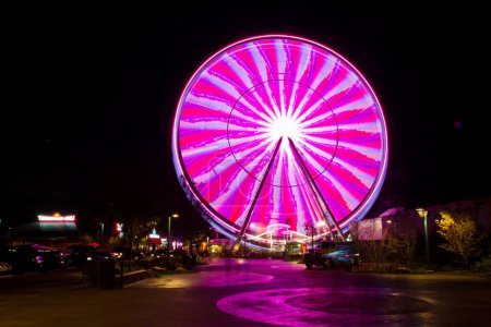 Photo for Vibrant long exposure photograph capturing the mesmerizing blur of a giant Ferris wheel at night in an urban entertainment area. Neon lights and dynamic motion evoke the excitement of city attractions - Royalty Free Image