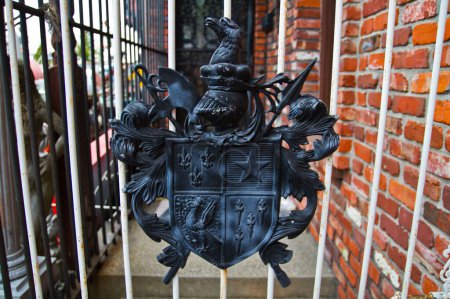 Photo for European Heraldry on Display: Ornate coat of arms adorns a white metal gate, featuring a shield with fleur-de-lis, a star, and a bird. Located in Louisville, Kentucky, this historical emblem - Royalty Free Image