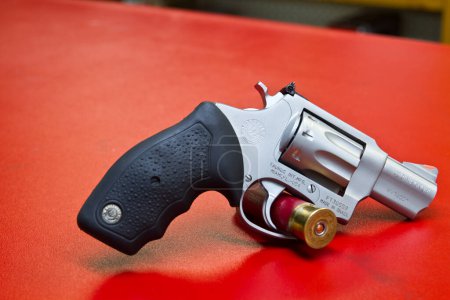 Photo for Ready for Action: A close-up view of a compact, modern .22 MAGNUM revolver with a shiny silver finish and black textured grip. The loaded weapon sits on a flat red surface, emphasizing its potential - Royalty Free Image