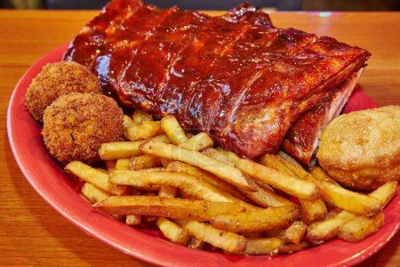 Photo for Indulge in a mouth-watering BBQ feast with glazed pork ribs, golden fries, and fried sides, served on a vibrant red plate. Perfect for showcasing American comfort food at its best. Culinary - Royalty Free Image