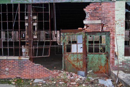 Photo for Decaying urban facade in Indiana, Warsaw: Explore the haunting beauty of an abandoned building with a rusting green metal door, crumbling red and white bricks, and a barricaded window. The desolate - Royalty Free Image