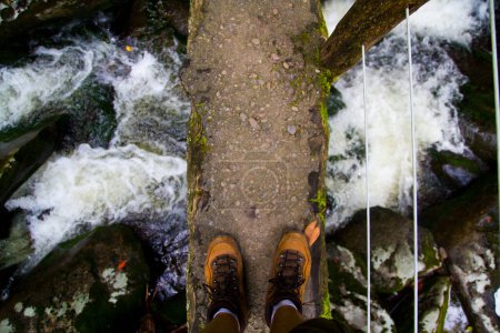 Journey into the Wild: A fearless adventurer crosses a weathered bridge over a rushing river, showcasing sturdy hiking boots against the untamed beauty of Gatlinburg, Tennessee. The perfect image for