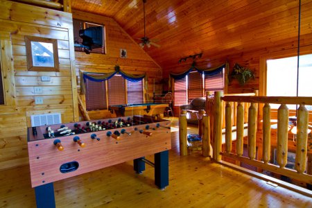 Experience the rustic charm of a cozy log cabin game room in Gatlinburg, Tennessee. This inviting space features a foosball table, billiards table, and a relaxing leather armchair, perfect for family