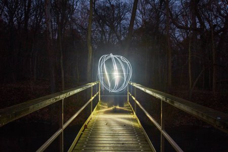 Photo for Enveloped by darkness, a wooden footbridge in a forest comes alive at night. A mesmerizing light painting creates a guiding orb, illuminating the path through the shadows. This captivating image - Royalty Free Image