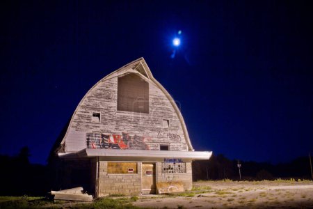 Téléchargez les photos : Capturer la beauté obsédante d'une ferme laitière abandonnée à Fort Wayne, Indiana. Des ombres éclairées au clair de lune dansent sur le toit de gambrel altéré, tandis que des graffitis racontent un passé oublié. Une image puissante pour - en image libre de droit