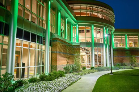 Photo for Captivating night view of a modern building in Fort Wayne, Indiana, illuminated by vibrant green lighting. The blend of contemporary design and traditional elements, including a curved glass facade - Royalty Free Image