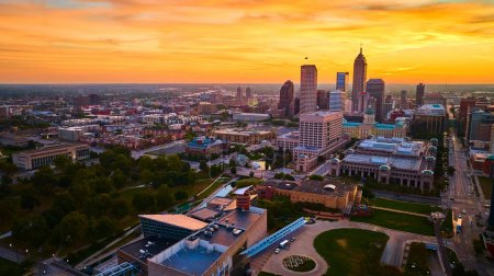 Golden Hour over Indianapolis - Vista aérea que muestra el horizonte de la ciudad con arquitectura moderna e histórica, espacios verdes y vías fluviales reflectantes al atardecer.