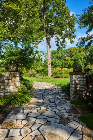 Photo for Serene stone pathway meandering through lush greenery of a well-maintained garden, with classical sculptures under a clear blue sky, Botanic Gardens, Elkhart, Indiana, 2023 - Royalty Free Image