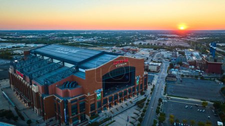 Téléchargez les photos : Coucher de soleil sur Lucas Oil Stadium, un lieu sportif emblématique d'Indianapolis, capturé en vue aérienne soulignant son toit rétractable, sa façade en brique et le paysage urbain. - en image libre de droit