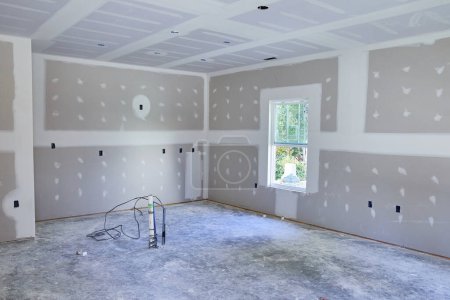 Photo for Daylight brightens a work-in-progress room in Fort Wayne, Indiana, featuring bare walls, a concrete floor, and a lone stepladder, symbolizing transformation and potential. - Royalty Free Image