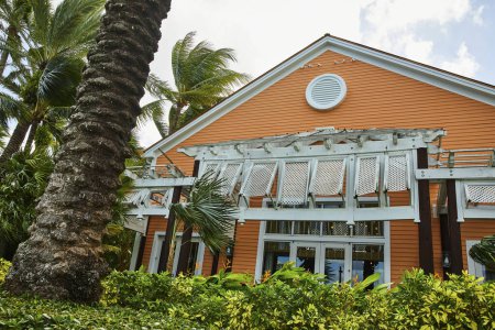 Tropical resort architecture in Nassau, Bahamas with vibrant orange facade, white gabled roof and porch, nestled amidst lush green palm trees on Paradise Island
