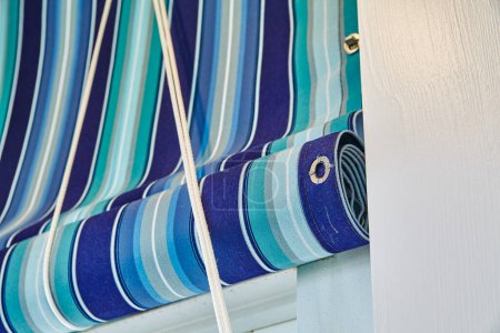 Téléchargez les photos : Rideaux rayés bleu vif soigneusement roulés, jumelés à une corde blanche par une journée ensoleillée dans un cadre résidentiel en Indiana, mettant en valeur la décoration extérieure et la protection solaire - en image libre de droit