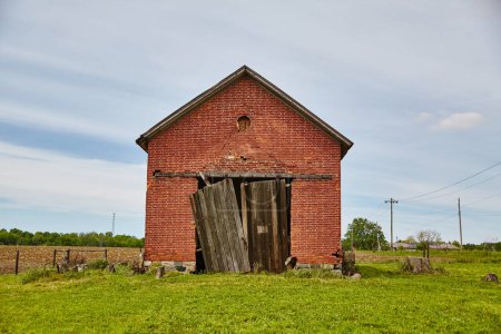 Foto de Granero de ladrillo abandonado en Auburn, Indiana, se levanta contra un cielo azul, lo que refleja la decadencia rural y el paso del tiempo en un campo tranquilo. - Imagen libre de derechos