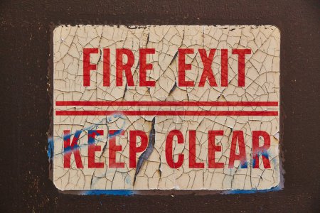 Vintage fire exit sign with peeling paint on a dark wall, symbolizing neglect, from the abandoned Riverside Hospital in Toledo, Ohio.