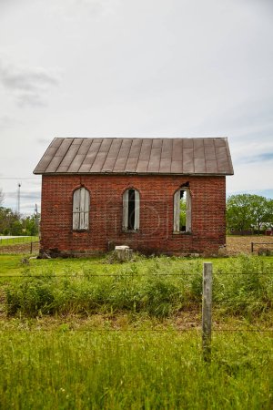 Foto de Edificio abandonado de ladrillo rojo en Auburn, Indiana, con césped cubierto bajo un cielo nublado. - Imagen libre de derechos