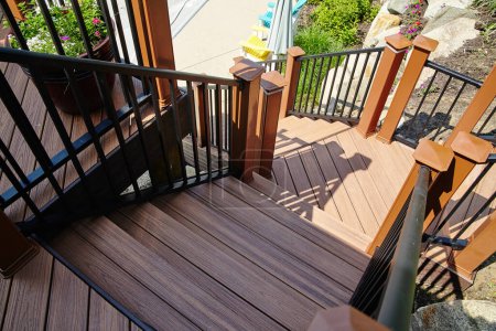 Serene wooden deck with modern metal railing and staircase, bathed in sunlight, set against a landscaped garden in Churubusco, Indiana.
