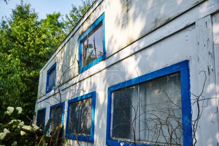 Téléchargez les photos : Abandonné Indiana Fun Spot montagnes russes bâtiment en 2015, incarnation de la décomposition rurale avec les murs blancs altérés, cadres de fenêtre bleu ébréché, et les natures récupérer. - en image libre de droit
