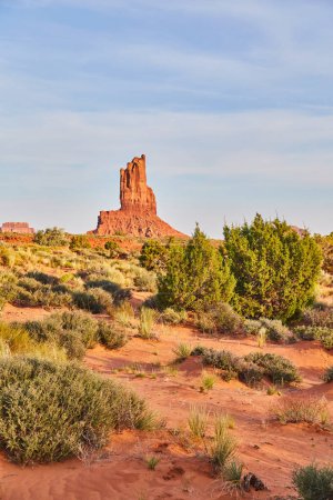 Photo for Golden Hour at Monument Valley, 2016 - Majestic sandstone butte rises against clear sky amid lush desert vegetation in Arizonas iconic desert landscape. - Royalty Free Image
