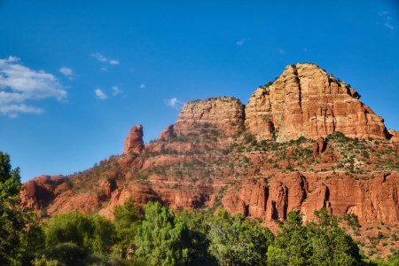 Téléchargez les photos : Vue diurne vibrante de 2016 de formations rocheuses rouges frappantes dominant un paysage verdoyant sous un ciel bleu clair à Sedona, Arizona - en image libre de droit