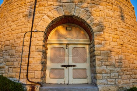 Téléchargez les photos : Lever de soleil sur une porte en bois voûtée historique à Ypsilanti, Michigan, soulignant le contraste de la lumière de l'heure dorée sur l'architecture en pierre robuste - en image libre de droit