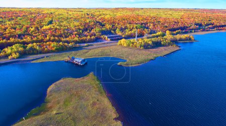 Aerial view of vibrant autumn foliage in Houghton, Michigan, contrasting with blue water and an abandoned Quincy Dredge, a symbol of decay overtaken by natures beauty