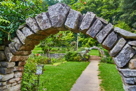 Arco de piedra en Spring Mills State Park, Indiana enmarcando un exuberante sendero de jardín, un símbolo de tranquilidad, historia y arquitectura.