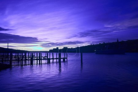 Crepúsculo reflexión sobre el agua tranquila en Houghton Docks, Michigan, con sereno paseo marítimo, barco amarrado, y silueta del horizonte de la ciudad