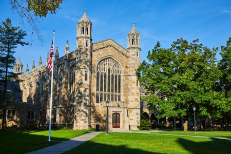 Universitätskapelle im gotischen Stil in Ann Arbor, Michigan unter strahlend blauem Himmel mit aufwändigem Mauerwerk und amerikanischer Flagge