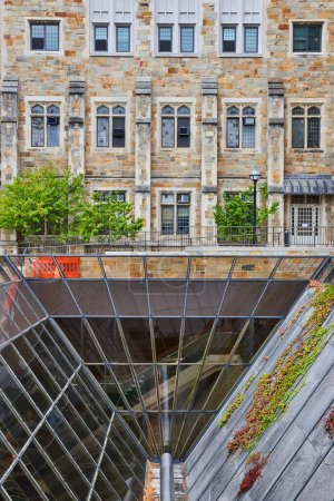 Blend of historical and modern architecture at University of Michigan Law Quadrangle, featuring an old stone building juxtaposed with a modern glass structure, on an overcast day