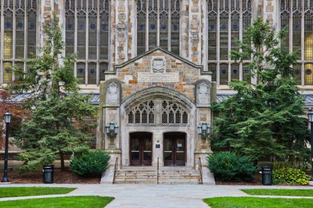 Gothic-style University of Michigan Law Quadrangle entrance with intricate wooden doors, ornate stone archway, and surrounding greenery