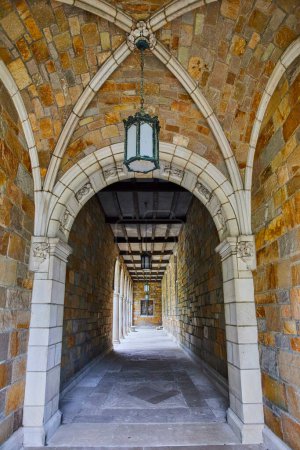 Stone corridor architecture showcasing medieval aesthetics at the University of Michigan Law Quadrangle, featuring a hanging antique lantern and wooden ceiling beams