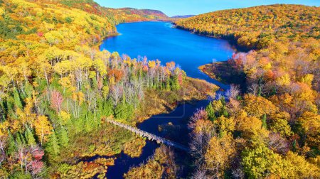 Aerial view of a vibrant autumn landscape with a wooden footbridge over a winding river, captured in Lake in the Clouds, Michigan, 2017.