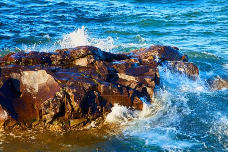 Sonnenbeschienene Felsklippen treffen bei Eagle Harbor, Lake Superior, Michigan, auf krachende Wellen und zeigen die rohe Kraft und Schönheit der Natur.