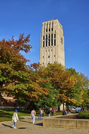 Photo for Students stroll under the historic Burton Memorial Tower amid a vibrant autumn setting at the University of Michigan, Ann Arbor, embodying the essence of college life and academia. - Royalty Free Image