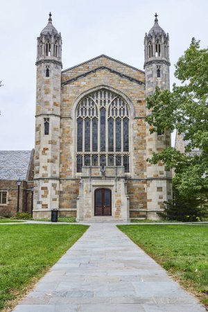 Gotische Steinkirche mit Buntglasfenster und Zwillingstürmen an der University of Michigan, Ann Arbor, Blick über einen grünen Rasen und gepflasterten Weg.