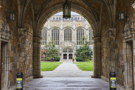 Photo for View through ornate archway at the historic University of Michigan Law Quadrangle, capturing a student walking towards the grand Gothic building, surrounded by lush greenery. - Royalty Free Image