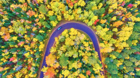 Aerial view of a lone vehicle traversing a vibrant autumn-hued forest on a winding road in Copper Harbor, Michigan, captured by a DJI Phantom 4 drone in 2017.