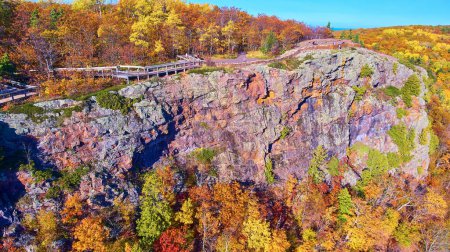 Autumnal vista at Lake in the Clouds, Michigan, captured by aerial drone in 2017 revealing rugged cliffs, vibrant fall foliage, and a winding wooden boardwalk.
