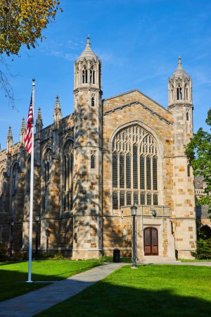 Gotische Steinkirche mit amerikanischer Flagge an der University of Michigan, Ann Arbor, die unter klarem blauen Himmel komplexe Architektur und historische Bedeutung präsentiert.