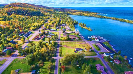 Aerial view of Copper Harbor in Michigan, showcasing vibrant autumn foliage, serene lake waters, and tranquil small-town life.